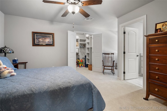 bedroom featuring visible vents, a walk in closet, light carpet, a closet, and a ceiling fan