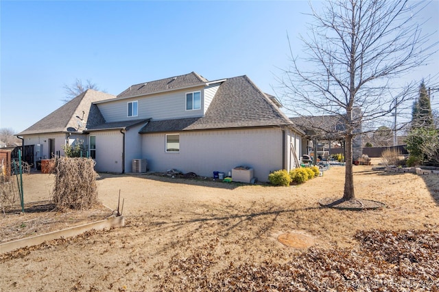 rear view of house featuring cooling unit, fence, brick siding, and roof with shingles