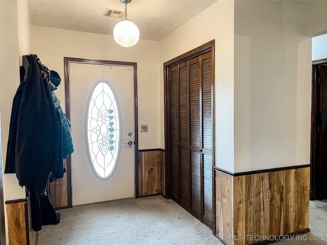 entryway with wooden walls, visible vents, carpet, wainscoting, and a textured ceiling