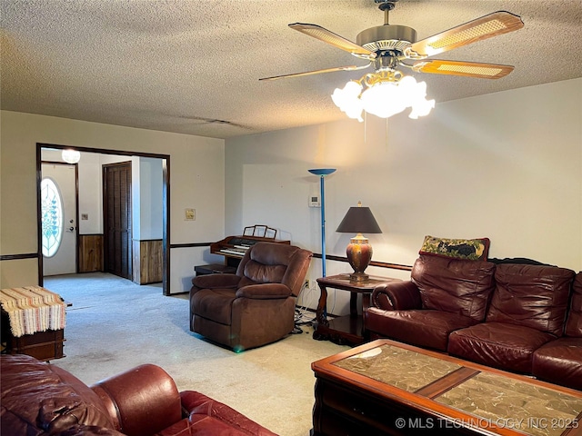 living room with carpet flooring, a textured ceiling, a ceiling fan, and a wainscoted wall