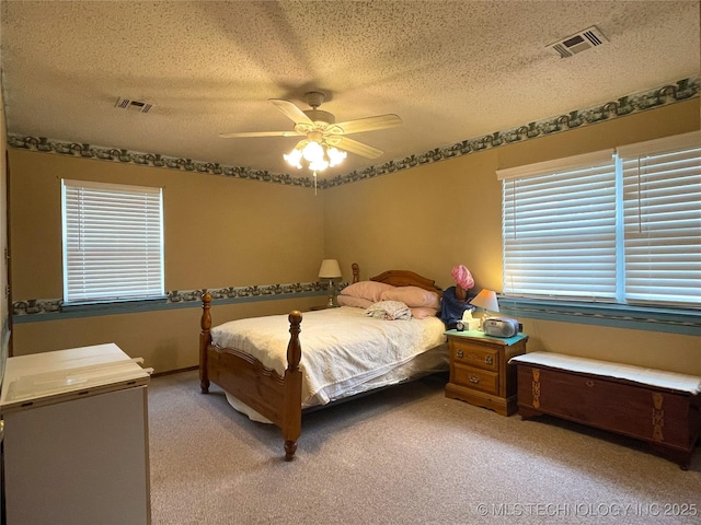 bedroom with light colored carpet, a ceiling fan, visible vents, and a textured ceiling