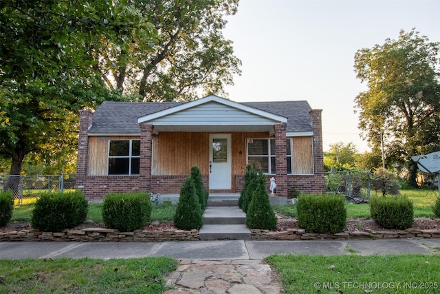 view of front of house featuring brick siding, a chimney, roof with shingles, and fence