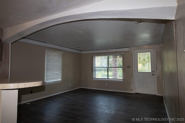 unfurnished living room featuring baseboards, arched walkways, and dark wood-type flooring