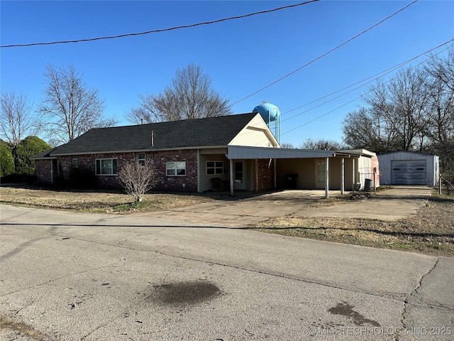 ranch-style house featuring an outbuilding, an attached carport, concrete driveway, brick siding, and a shingled roof