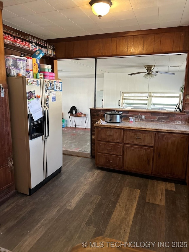 kitchen featuring wooden walls, dark wood-type flooring, ceiling fan, and white fridge with ice dispenser