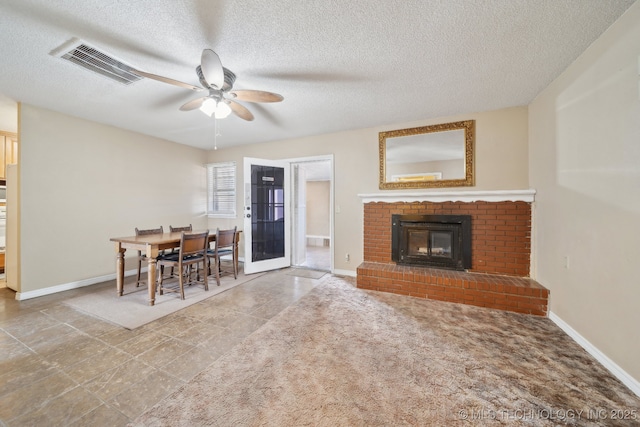 living room featuring visible vents, a fireplace, a textured ceiling, and a ceiling fan