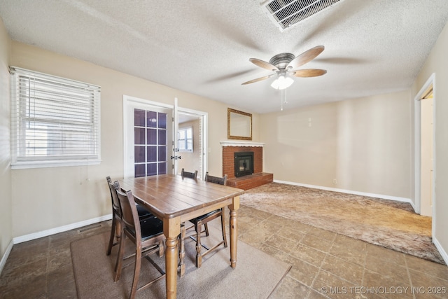 dining room with visible vents, a ceiling fan, a textured ceiling, baseboards, and a brick fireplace