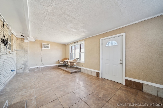 tiled entryway featuring a wall unit AC, baseboards, brick wall, and a textured ceiling