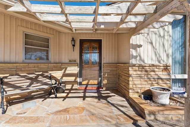 property entrance with stone siding and a pergola