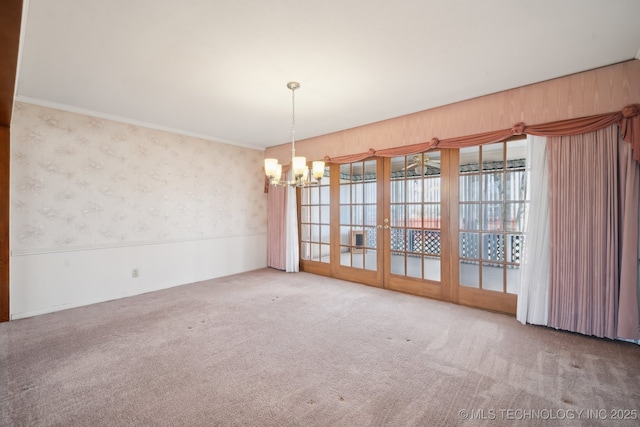 carpeted empty room with a notable chandelier, ornamental molding, and wallpapered walls