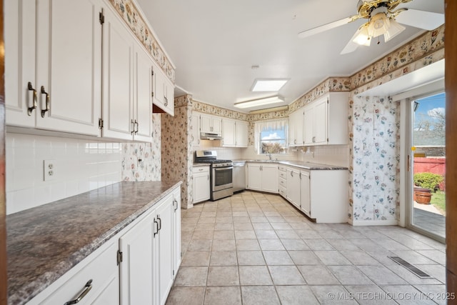 kitchen featuring a sink, under cabinet range hood, stainless steel gas range oven, white cabinetry, and backsplash