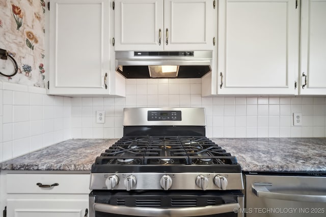 kitchen featuring under cabinet range hood, decorative backsplash, dark stone countertops, gas stove, and white cabinetry