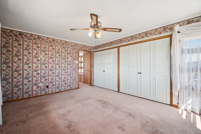 unfurnished bedroom featuring wallpapered walls, baseboards, multiple closets, carpet floors, and ornamental molding