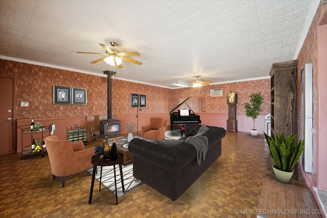 living room with wallpapered walls, a wood stove, ornamental molding, and ceiling fan