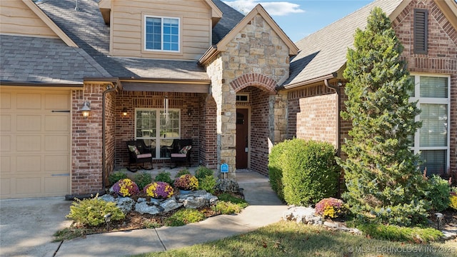 property entrance featuring brick siding, roof with shingles, covered porch, stone siding, and an attached garage