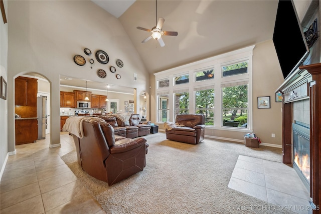 living area featuring a tiled fireplace, light colored carpet, light tile patterned floors, arched walkways, and high vaulted ceiling