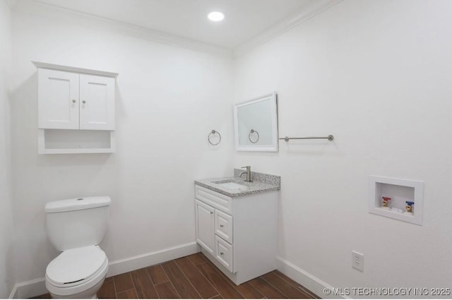 bathroom featuring wood finish floors, toilet, crown molding, baseboards, and vanity