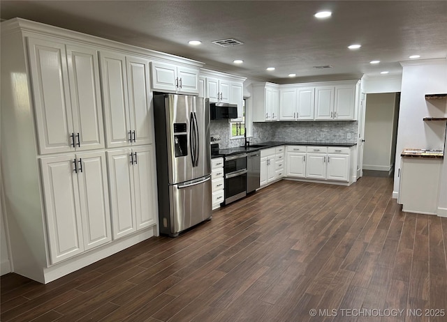 kitchen with dark wood-type flooring, a sink, dark countertops, appliances with stainless steel finishes, and decorative backsplash