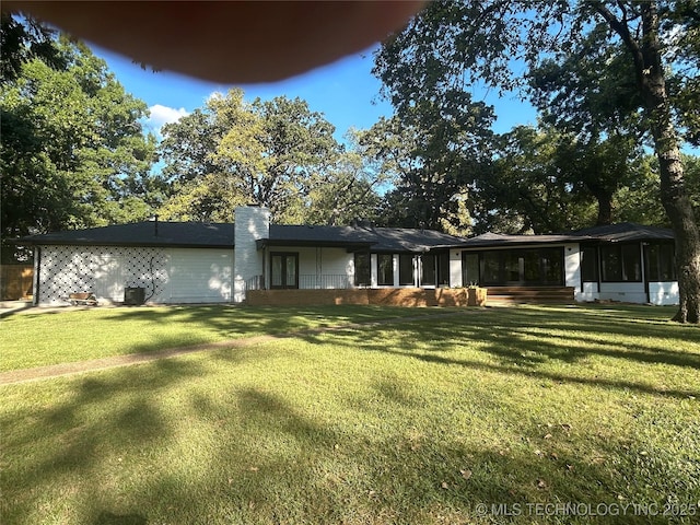 rear view of property featuring a chimney, a yard, and a sunroom