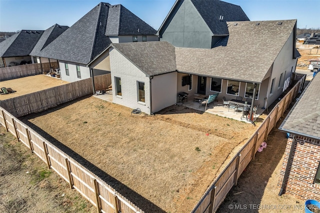 rear view of house featuring a fenced backyard, stucco siding, a shingled roof, and a patio