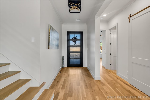 foyer entrance featuring stairway, baseboards, ornamental molding, a barn door, and light wood-type flooring