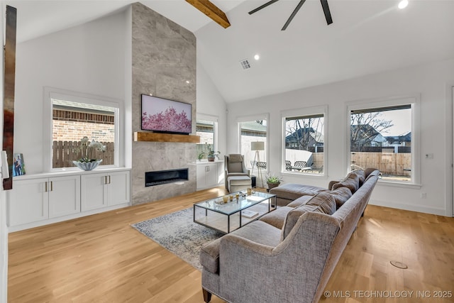 living room featuring baseboards, visible vents, high vaulted ceiling, light wood finished floors, and a tile fireplace