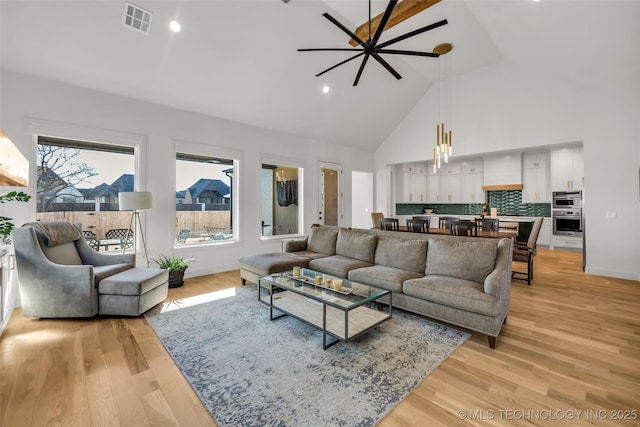 living area featuring baseboards, visible vents, light wood finished floors, and high vaulted ceiling