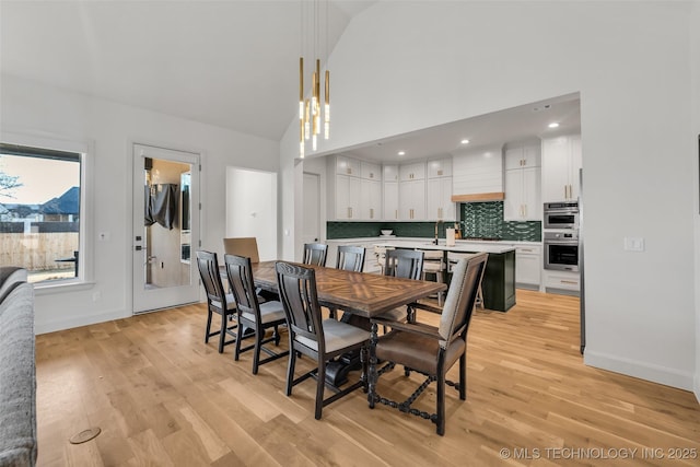 dining room featuring light wood-style flooring, baseboards, and high vaulted ceiling