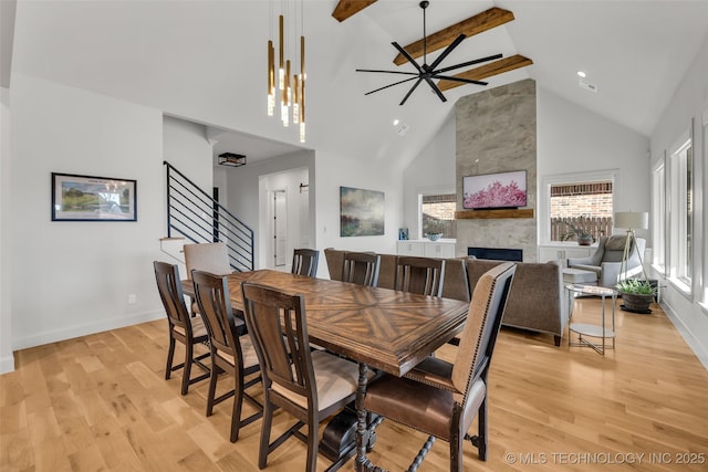 dining space with baseboards, high vaulted ceiling, stairs, light wood-style floors, and a large fireplace