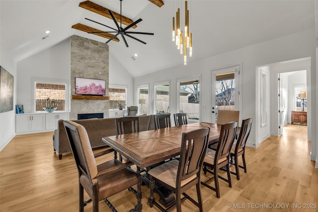 dining space featuring high vaulted ceiling, beam ceiling, light wood-style floors, and a fireplace