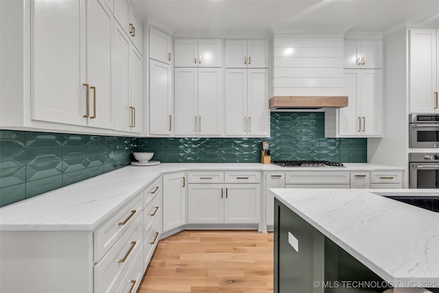 kitchen featuring light stone counters, light wood-style floors, appliances with stainless steel finishes, and white cabinets