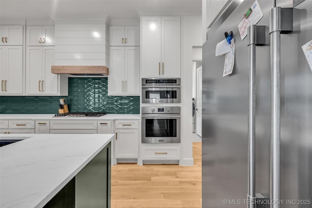 kitchen with light wood finished floors, backsplash, appliances with stainless steel finishes, and white cabinetry