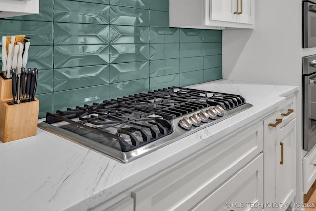 kitchen with light stone counters, backsplash, white cabinetry, and stainless steel appliances