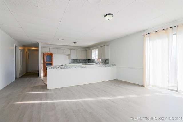 kitchen featuring tasteful backsplash, a peninsula, gray cabinetry, and light wood-style floors