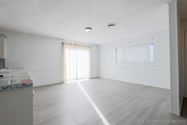 spare room featuring baseboards, a paneled ceiling, and light wood-style floors