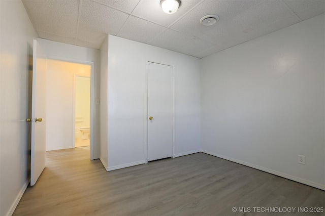 unfurnished bedroom with a paneled ceiling, baseboards, and wood finished floors