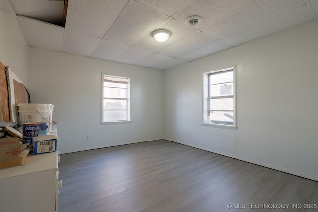 empty room with plenty of natural light, wood finished floors, baseboards, and a drop ceiling