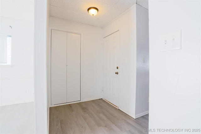 corridor with a drop ceiling, baseboards, and light wood-style floors