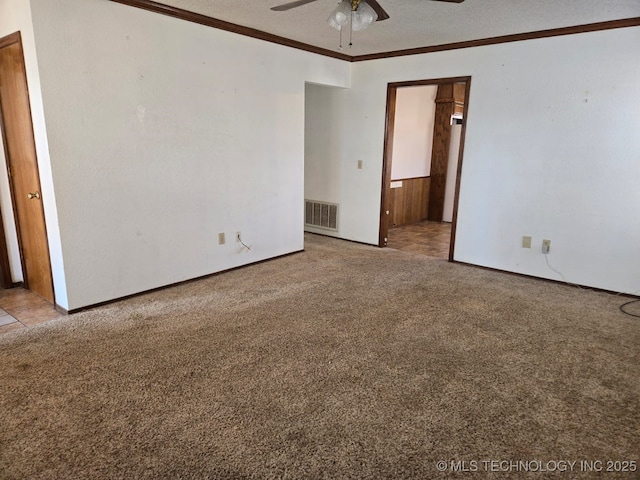 carpeted empty room with ceiling fan, visible vents, and ornamental molding