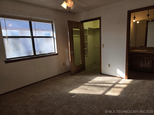 unfurnished bedroom with carpet floors, ensuite bath, a sink, a textured ceiling, and a walk in closet