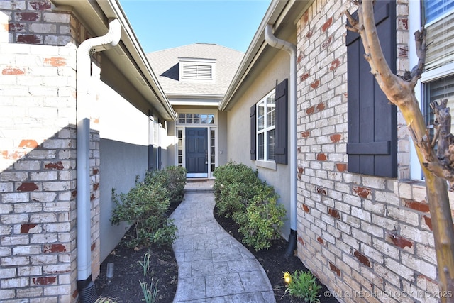 doorway to property featuring brick siding and a shingled roof