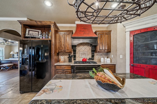 kitchen with wall oven, custom range hood, decorative backsplash, black fridge, and a ceiling fan