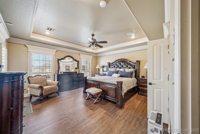 bedroom featuring a tray ceiling, crown molding, wood finished floors, and visible vents