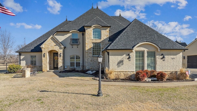 french country inspired facade featuring brick siding, stone siding, a front yard, and roof with shingles