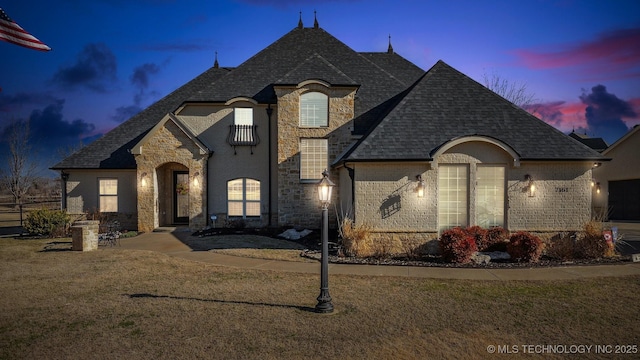 french country home with stone siding, a lawn, and a shingled roof