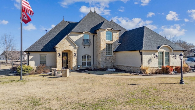 french provincial home with a front lawn, stone siding, and roof with shingles