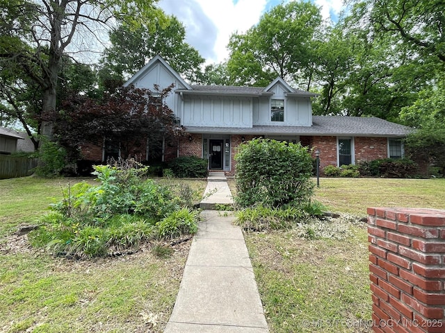 traditional home featuring brick siding, board and batten siding, a front yard, and roof with shingles