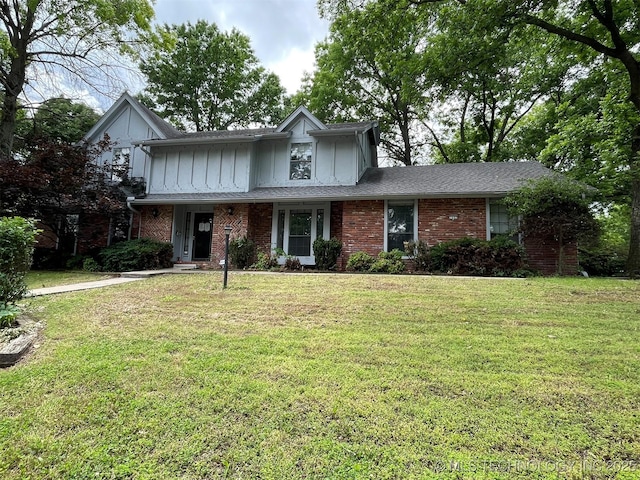 traditional-style house with board and batten siding, a front yard, brick siding, and a shingled roof