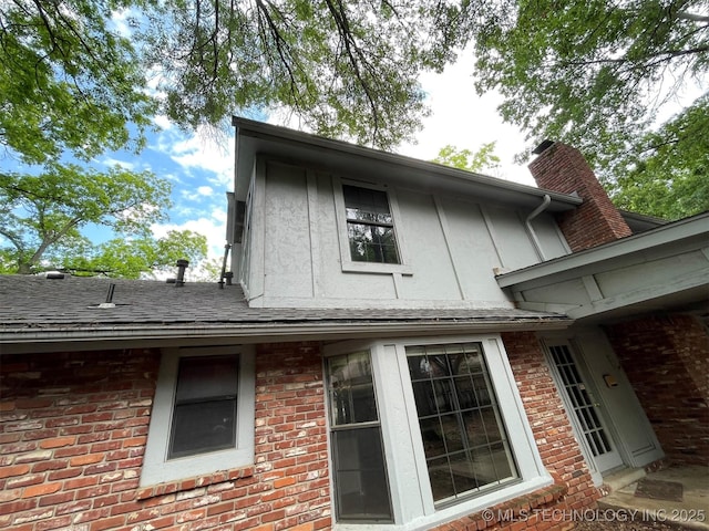 view of side of property with brick siding, a chimney, and roof with shingles