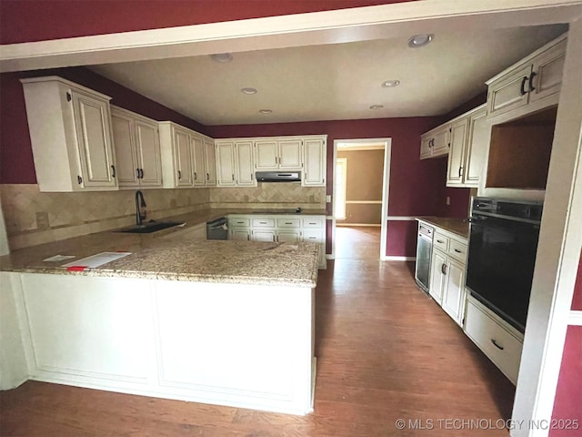 kitchen featuring a peninsula, a sink, under cabinet range hood, dishwasher, and black oven